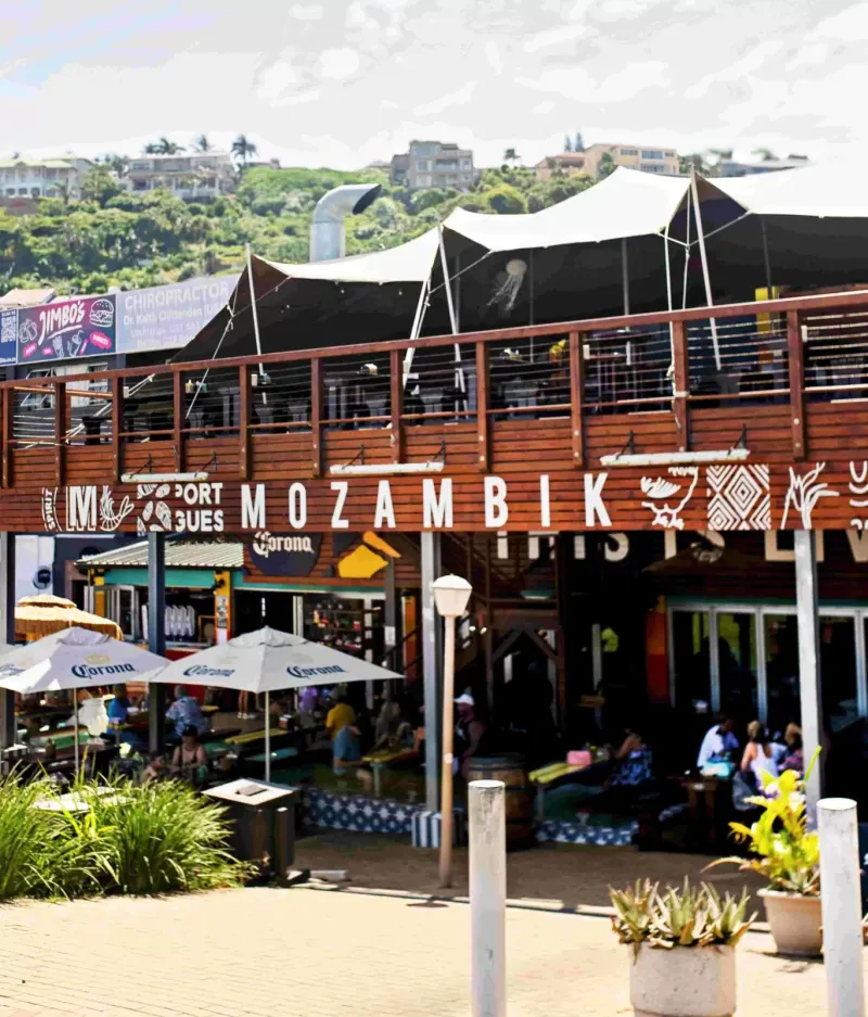 Mozambik restaurant exterior with outdoor seating under Corona umbrellas and lush hillside behind