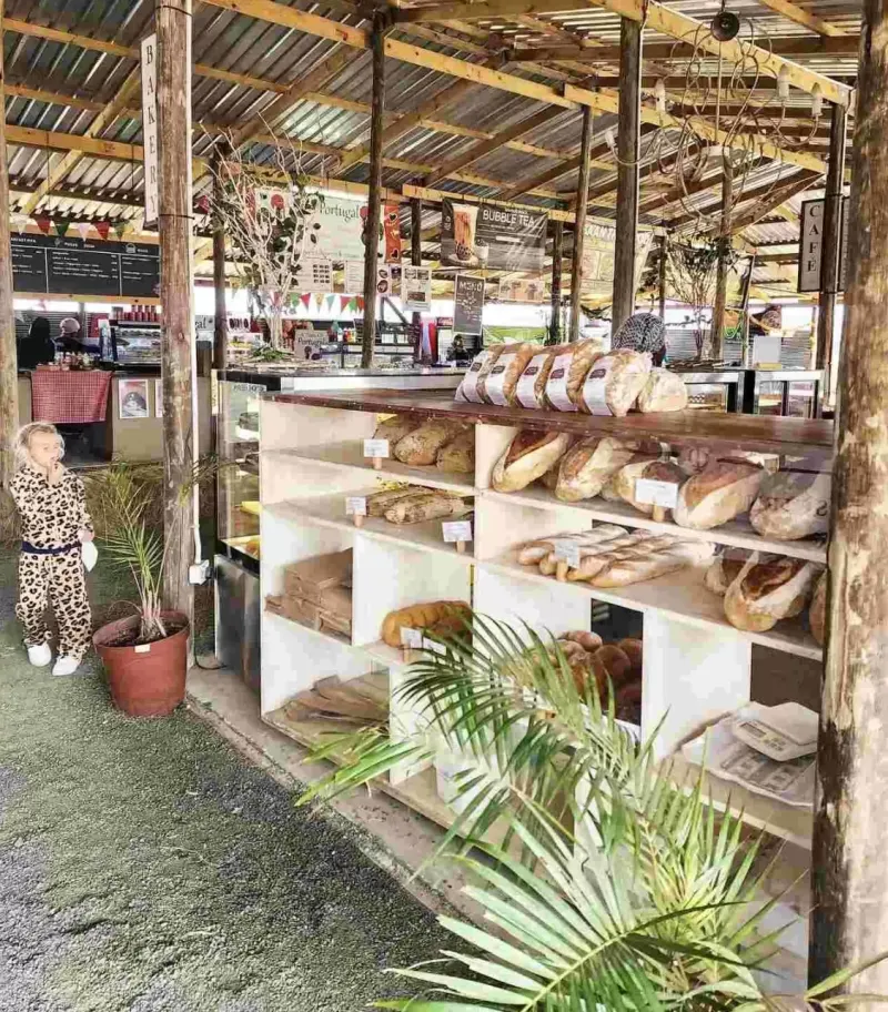 Young child in leopard print outfit stands beside open-air bakery shelves filled with artisan breads