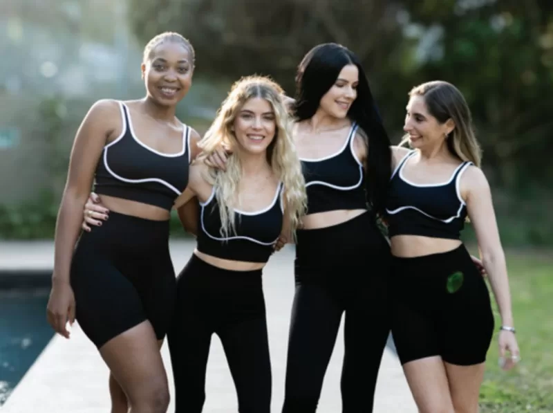 four women in matching black activewear posing together outdoors near a pool